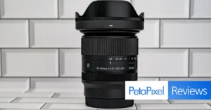 Об'єктив Sigma 20-60mm f/2.8-4 DG Contemporary стоїть вертикально на білому плитковому фоні, з логотипом PetaPixel Reviews у правому нижньому куті.