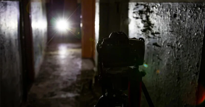 Фотографія камери на штативі, спрямованої на яскраве джерело світла в кінці темного, вузького коридору з текстурованими стінами.