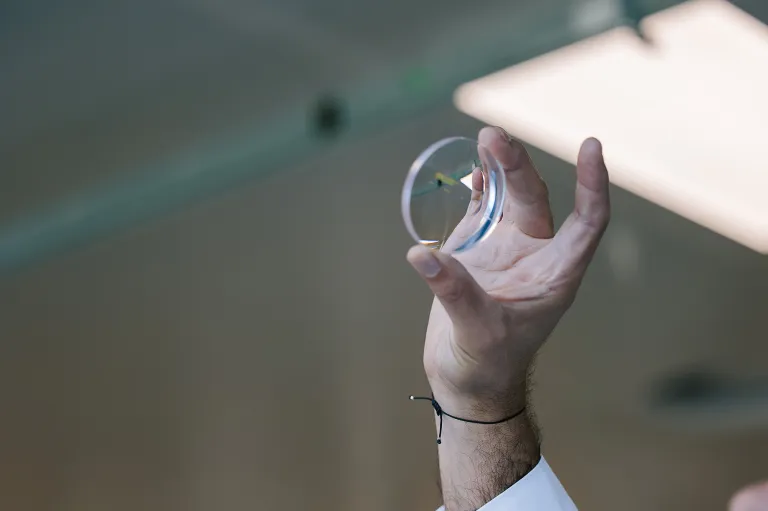 An uncut glasses lens held up by a lab technician