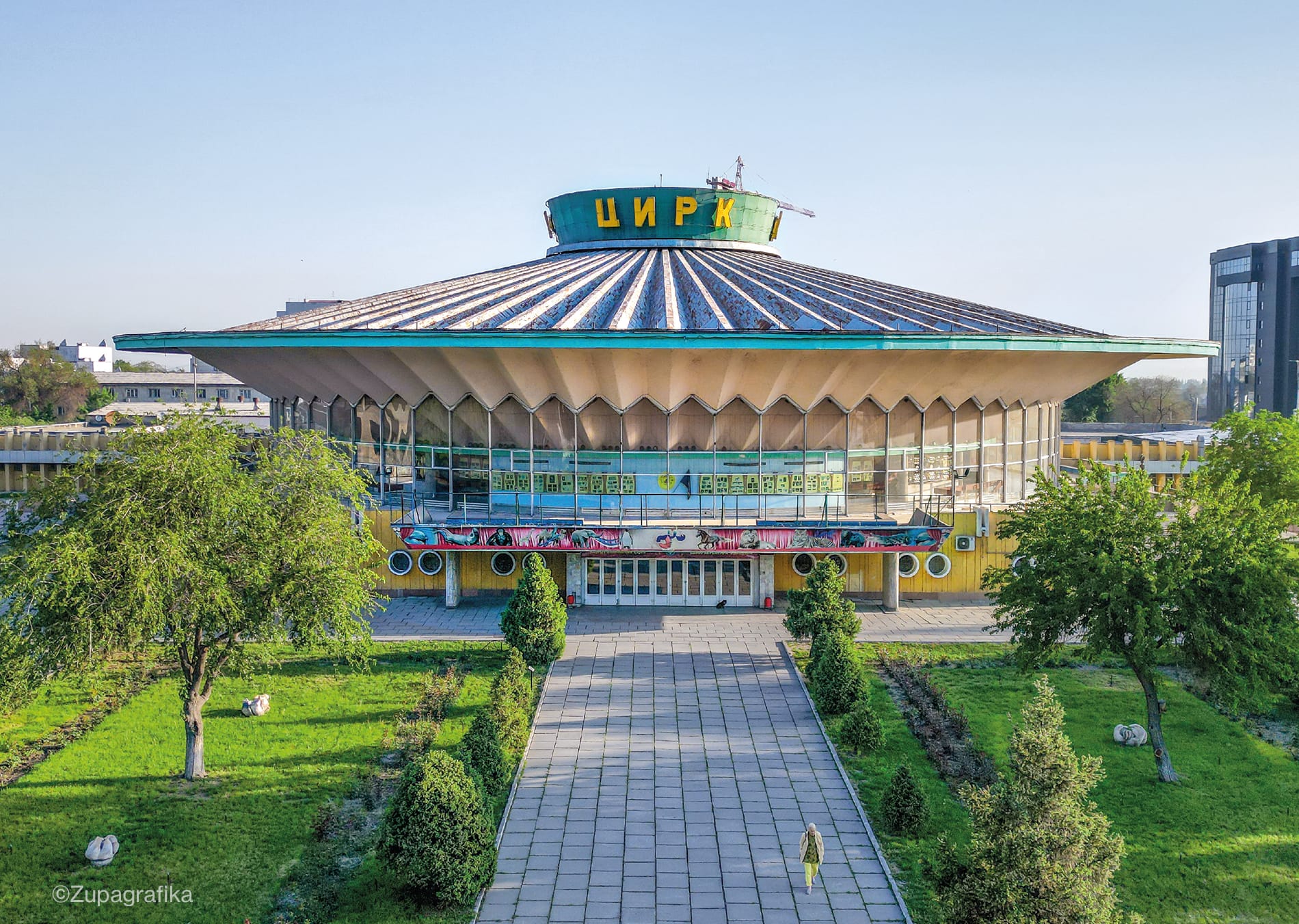 a modern, round arena building surrounded by greenery