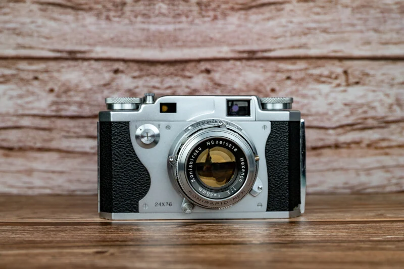 Вінтажна плівкова камера Konishiroku Hexanon 35mm розташована по центру на дерев'яній поверхні на фоні світлої текстури дерева.