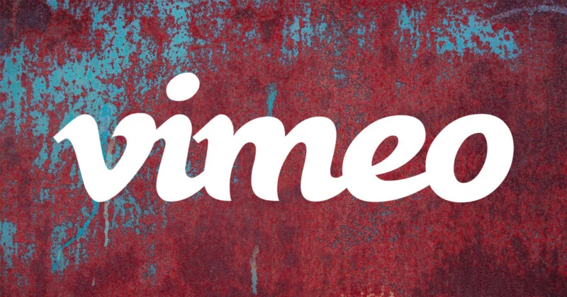 Білий логотип Vimeo розташований по центру на тлі старого, іржавого металу з плямами синьої фарби.