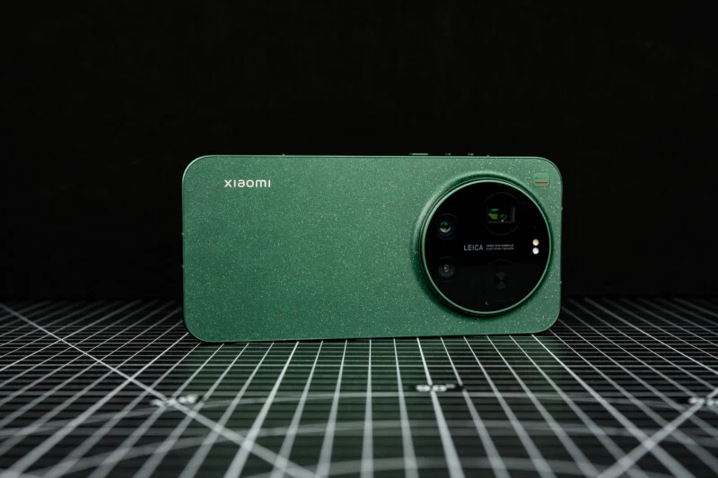 Зелений смартфон Xiaomi з великим модулем камери Leica розміщений на чорній поверхні з сітчастою основою, на темному тлі.