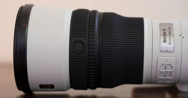 Крупний план бічного вигляду білого телеоб'єктива Sony FE 4.5/400 GM, що показує кільце фокусування, функціональну кнопку та перемикачі керування на корпусі.