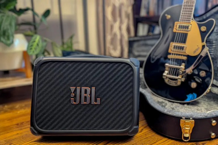 Чорний BandBox Trio з великим логотипом JBL на передньому плані, а за ним – гітара Gibson у футлярі.