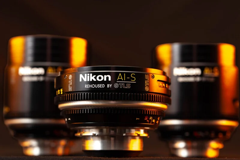 Три кінематографічні об'єктиви Nikon AI-S, перероблені TLS, розташовані на темній поверхні. Центральний об'єктив у різкості.