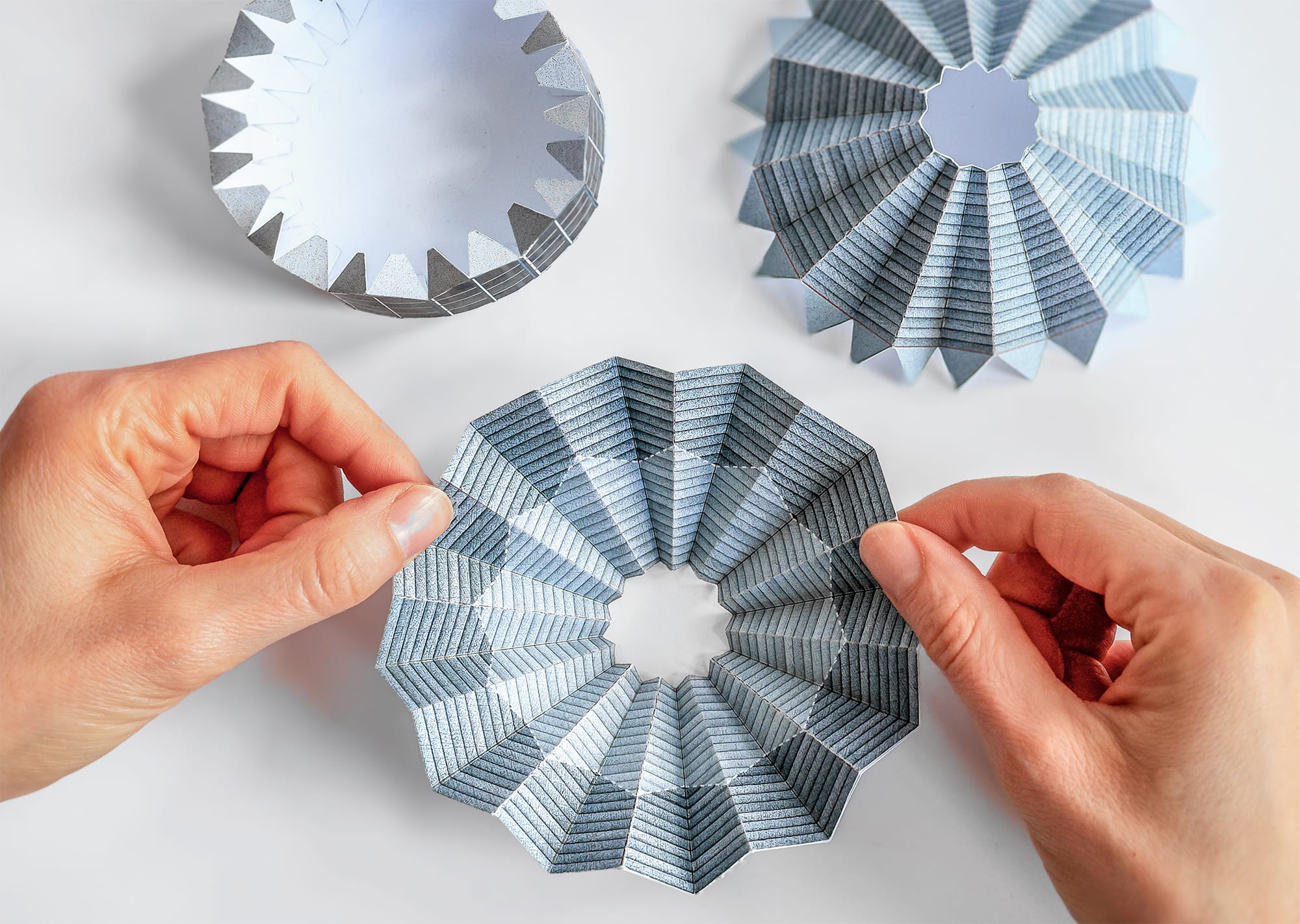 two hands manipulate a folded paper element that's part of a small building model