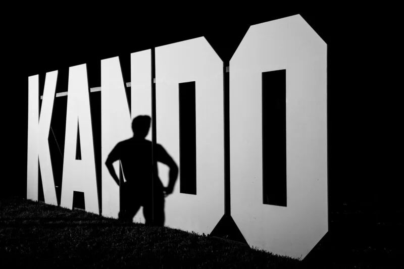 Чорно-біле фото тіні людини на великому білому знаку "KANDO".