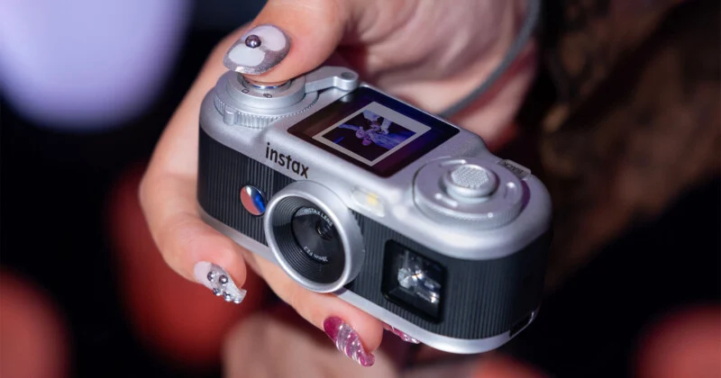 Людина тримає сріблясто-чорну цифрову камеру Instax, показуючи невелике фото на задньому екрані.