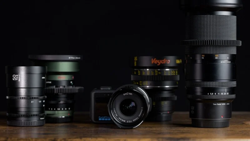 Колекція різноманітних об'єктивів для камер та камера GoPro, розташовані на дерев'яній поверхні на темному тлі.