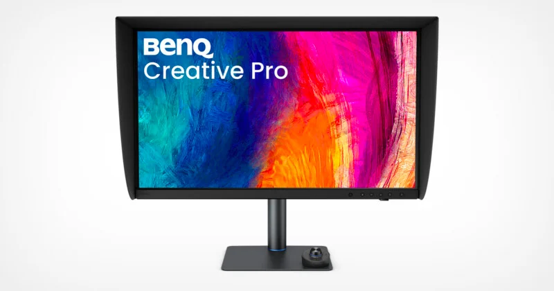 Монітор BenQ Creative Pro з ковпаком для захисту від світла стоїть на столі. На екрані відображається яскраве абстрактне зображення, а в основі пристрою розташований круглий регулятор.