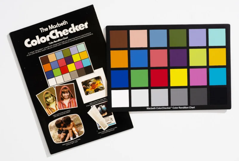 Діаграма Macbeth ColorChecker частково перекриває свою оригінальну чорну картонну упаковку з прикладами фотографій та описовим текстом.