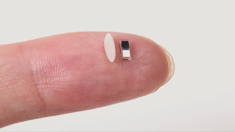 close up of finger balancing a grain of rice next to tiny pacemaker for size comparison
