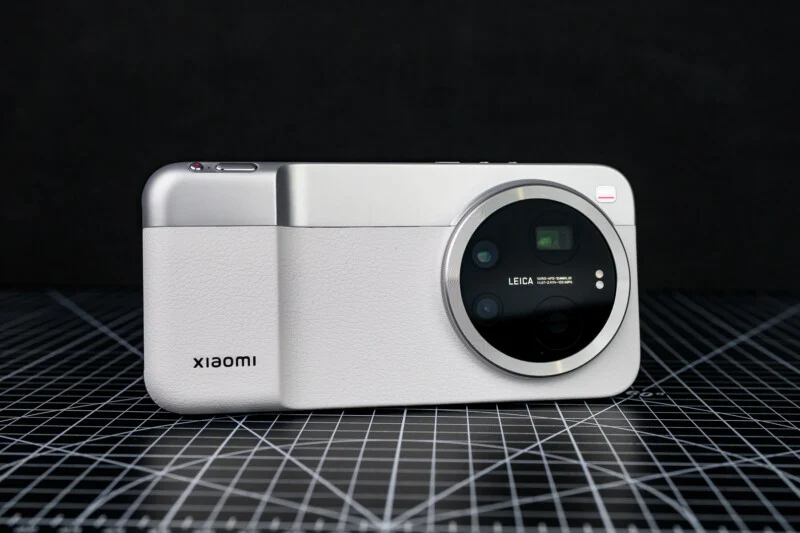 Сріблястий смартфон Xiaomi з великим круглим модулем камери Leica на задній панелі, розташований на чорній поверхні з сітчастою основою, на темному тлі.