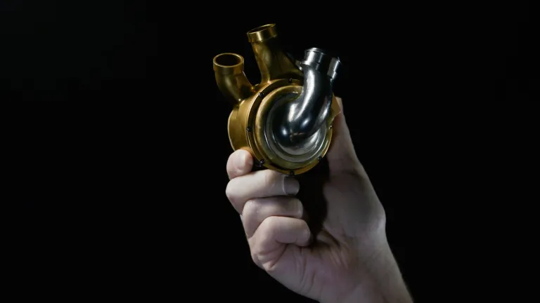 Hand holding titanium heart implant against black background