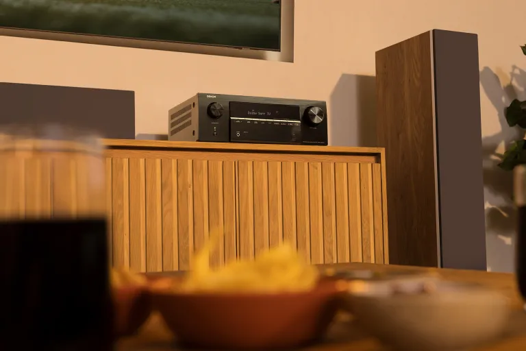 AV-ресивер Denon AVR-X2900 у чорному виконанні, розташований на дерев'яній тумбі у стилі середини століття, поруч із колонкою.