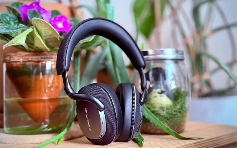 Black Bowers &amp; Wilkins Px7 S3 headphones sitting in front of colorful flowers on a bamboo table