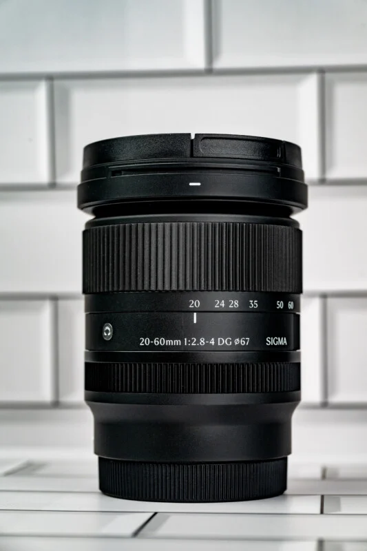 Чорний об'єктив Sigma 20-60mm 1:2.8-4 DG 67mm стоїть вертикально.