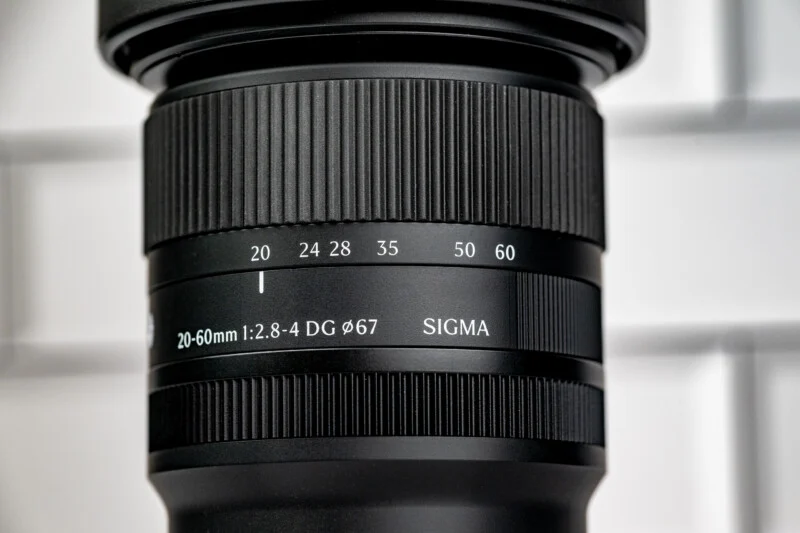 Макрофото чорного об'єктива Sigma 20-60mm, що показує позначки фокусної відстані та діаметр різьби фільтра 67 мм.