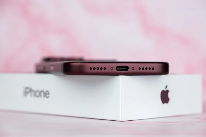 Темно-червоний смартфон лежить на білій коробці iPhone на рожевому мармуровому тлі.