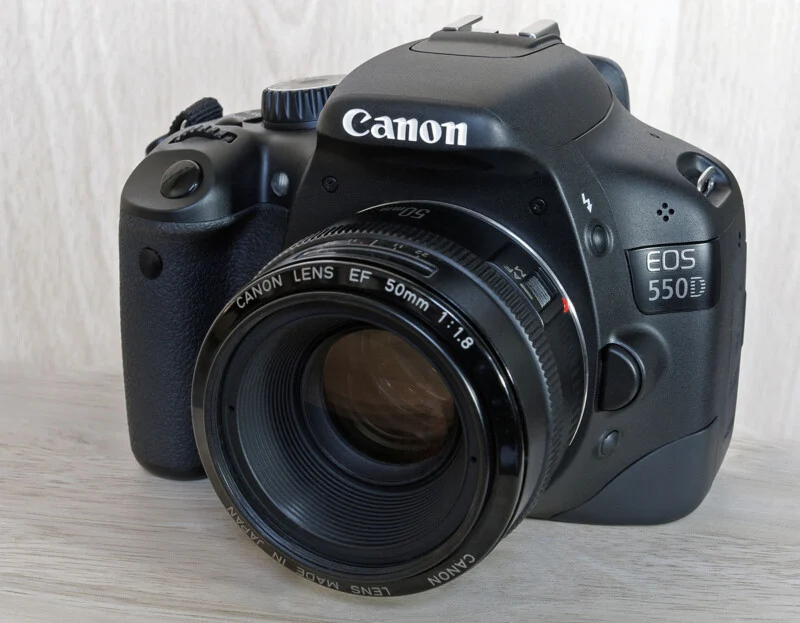Чорний дзеркальний фотоапарат Canon EOS 550D з об'єктивом 50mm f/1.8, встановлений на світлій дерев'яній поверхні.