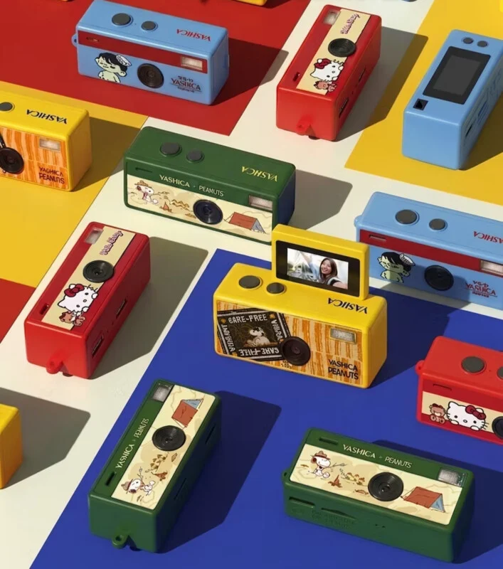 Яскраві камери Yashica з персонажами Peanuts у червоному, жовтому, зеленому та синьому кольорах розташовані на барвистому фоні з візерунками. Кожна камера має дизайн Peanuts або Hello Kitty, а одна жовта камера показує цифровий екран.
