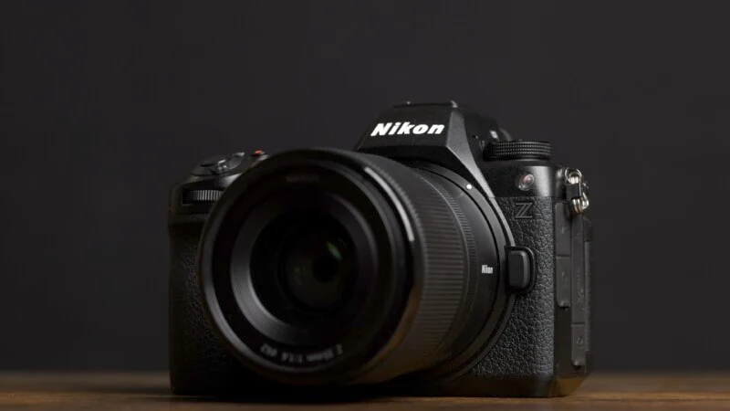 Фото камери Nikon серії Z з об'єктивом на дерев'яній поверхні на чорному тлі. Логотип Nikon видно на корпусі камери.