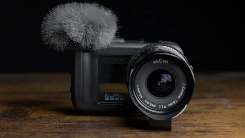 Камера GoPro з об'єктивом Laowa C-Dreamer 7.5mm та пухнастим вітрозахистом для мікрофона лежить на дерев'яній поверхні на чорному тлі.