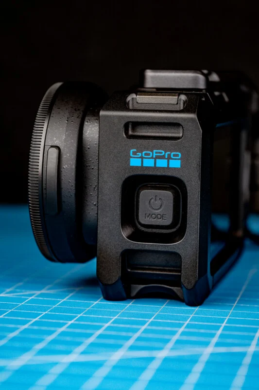 Чорний корпус камери GoPro з кнопкою живлення лежить на синьому сітчастому килимку на темному тлі.