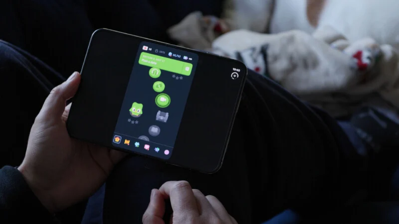 Людина тримає складаний смартфон, що відображає інтерфейс додатку Duolingo, показуючи шлях вивчення мови в процесі.